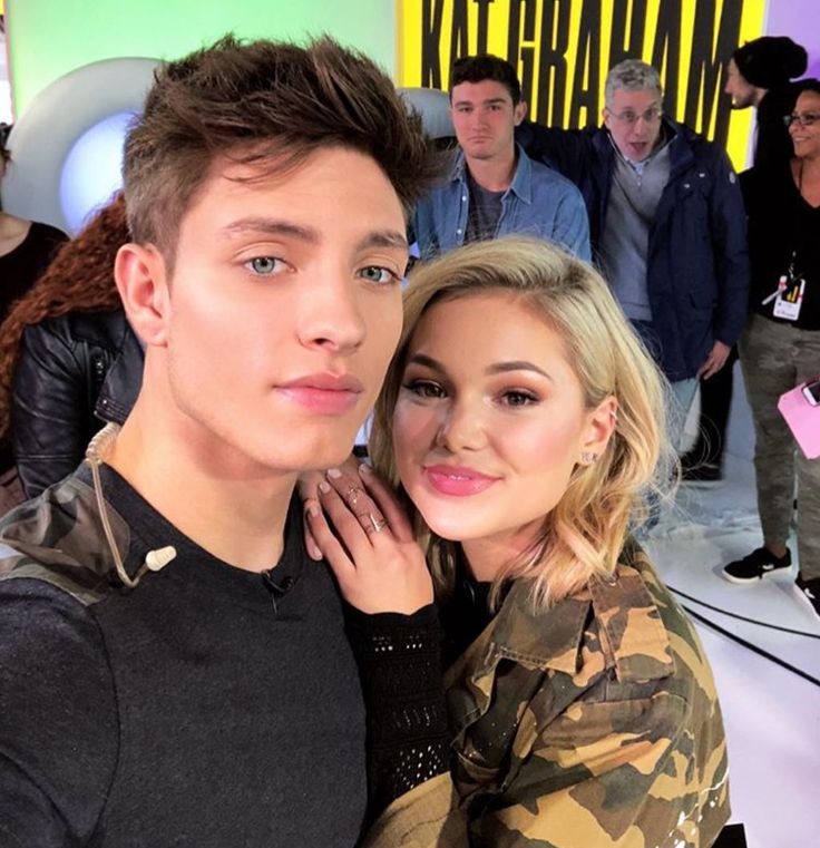 a young man and woman posing for a photo in front of a group of people