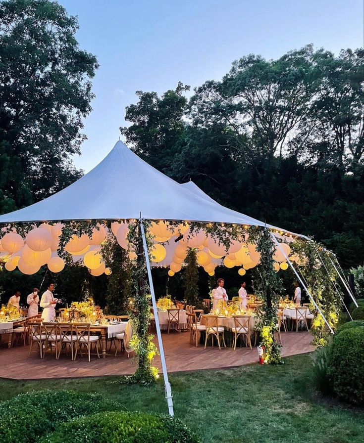 a large tent set up with tables and chairs for an outdoor party or gathering in the evening