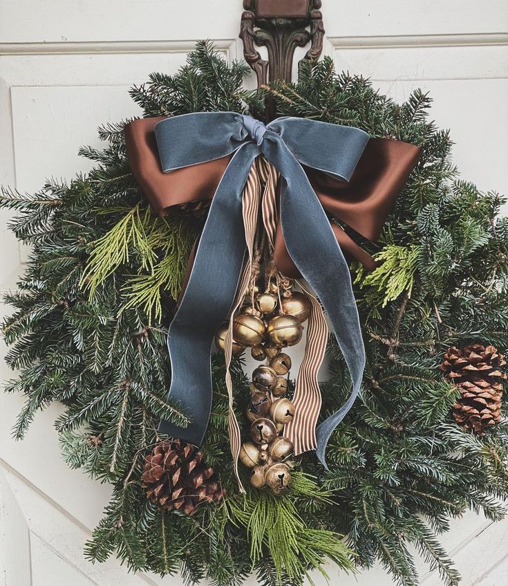 a christmas wreath with bells and pine cones hanging on the front door, decorated with blue ribbon