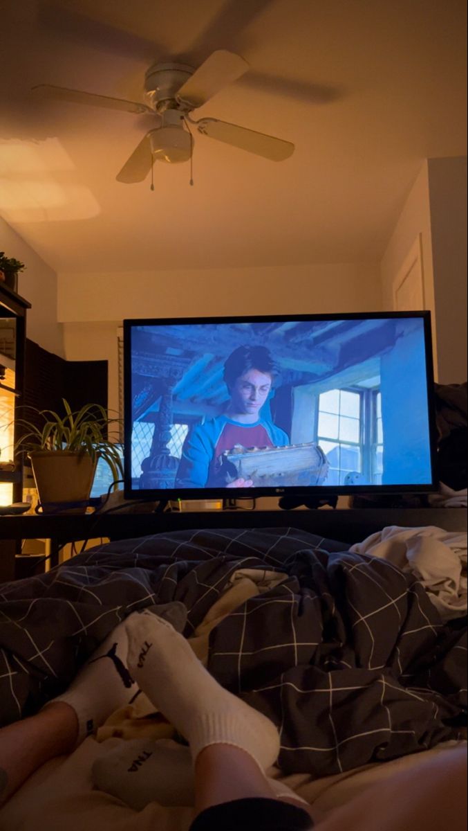 a person laying on a bed in front of a flat screen tv, with the television turned on