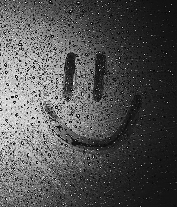 a smiley face drawn on the side of a window covered in raindrops and water droplets