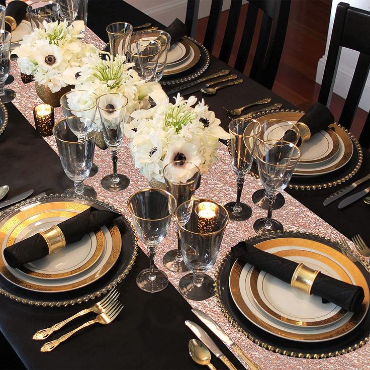 the table is set with black and gold plates, silverware, and white flowers