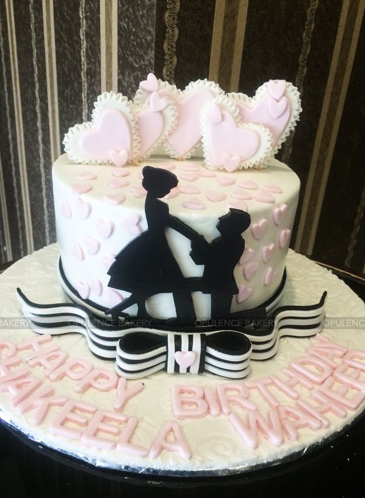 a wedding cake with pink and white frosting on the top is decorated with silhouettes of bride and groom