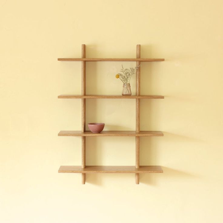 a wooden shelf with two vases on top and one flower in the middle, against a yellow wall