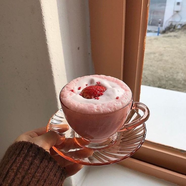 a person holding a drink in front of a window