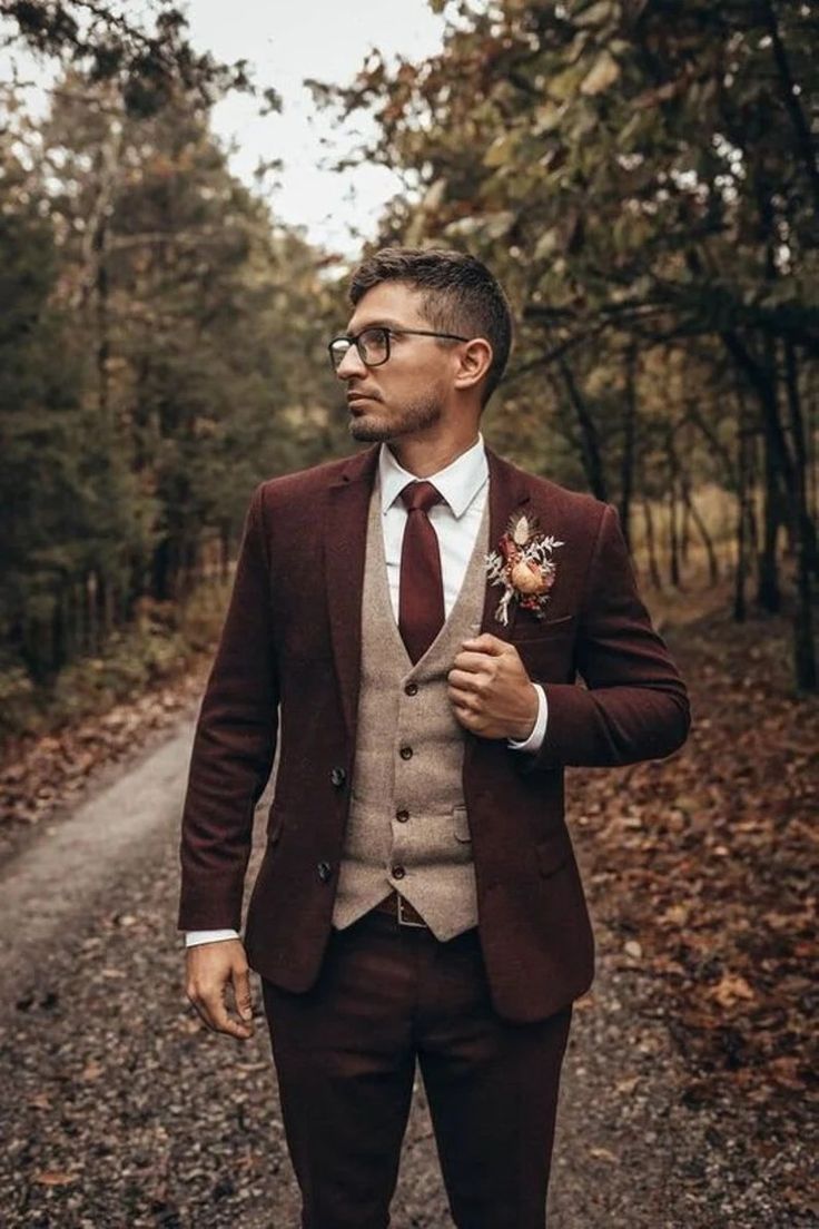 a man in a suit and tie standing on a dirt road with trees behind him