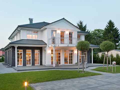 a large white house with lots of windows and lights on the front porch, surrounded by grass