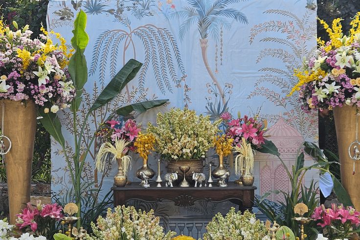 an arrangement of flowers and plants in front of a blue wall with gold vases