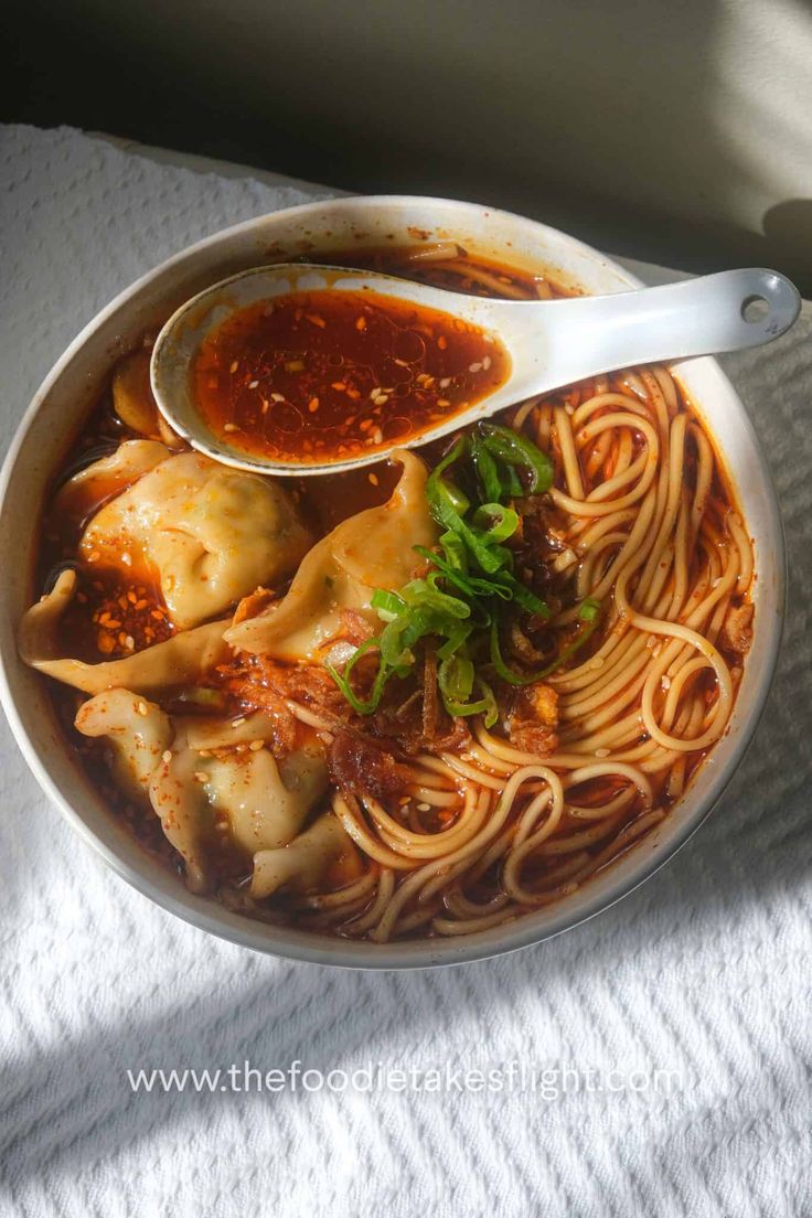 a bowl filled with noodles and sauce on top of a white cloth covered tablecloth