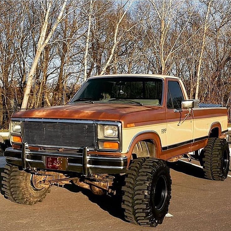 an orange and brown truck is parked in a parking lot next to some bare trees