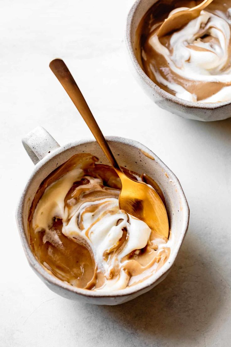 two cups filled with ice cream and caramel sauce on top of a white table