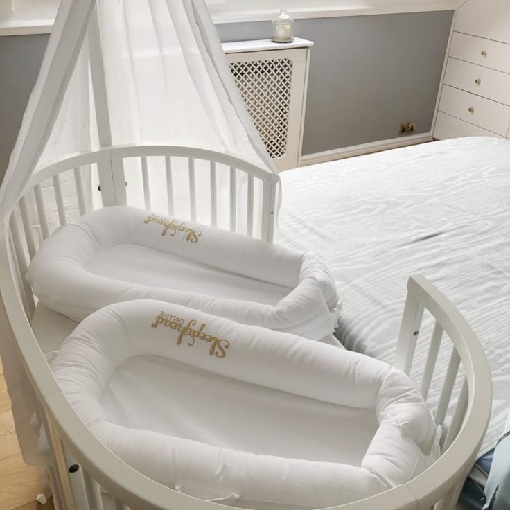 two baby cribs sitting next to each other on a bed in a room