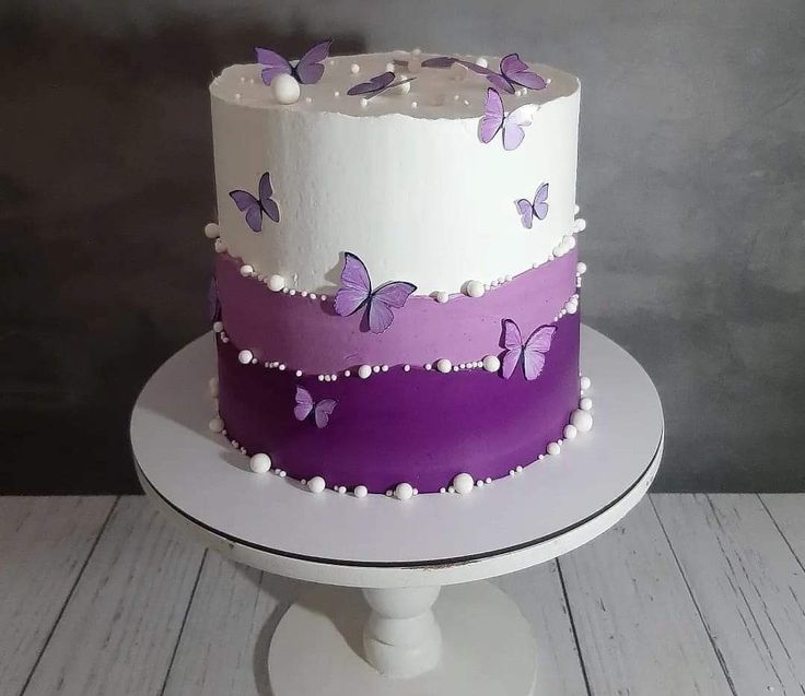 a three tiered cake with purple butterflies on the top and white frosting around it