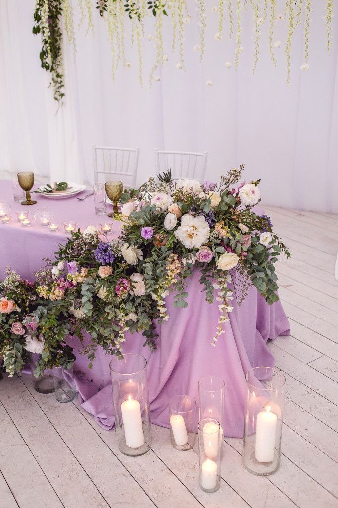 an arrangement of flowers and candles are on the floor next to a purple table cloth