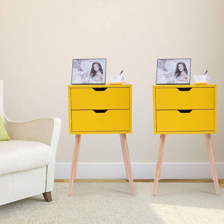 two yellow nightstands with pictures on them in front of a white chair and wall