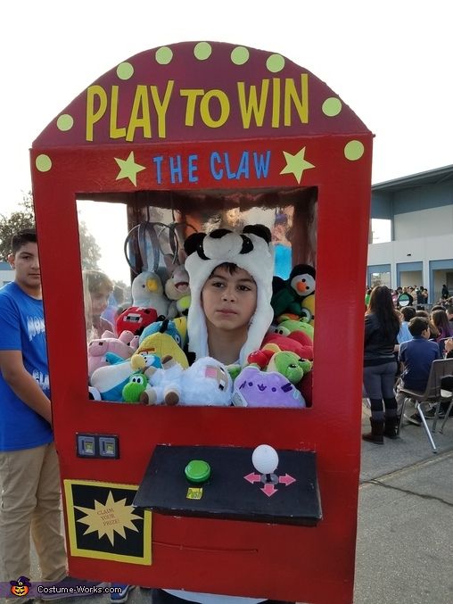 a young boy in a costume is playing the claw vending machine at an amusement park