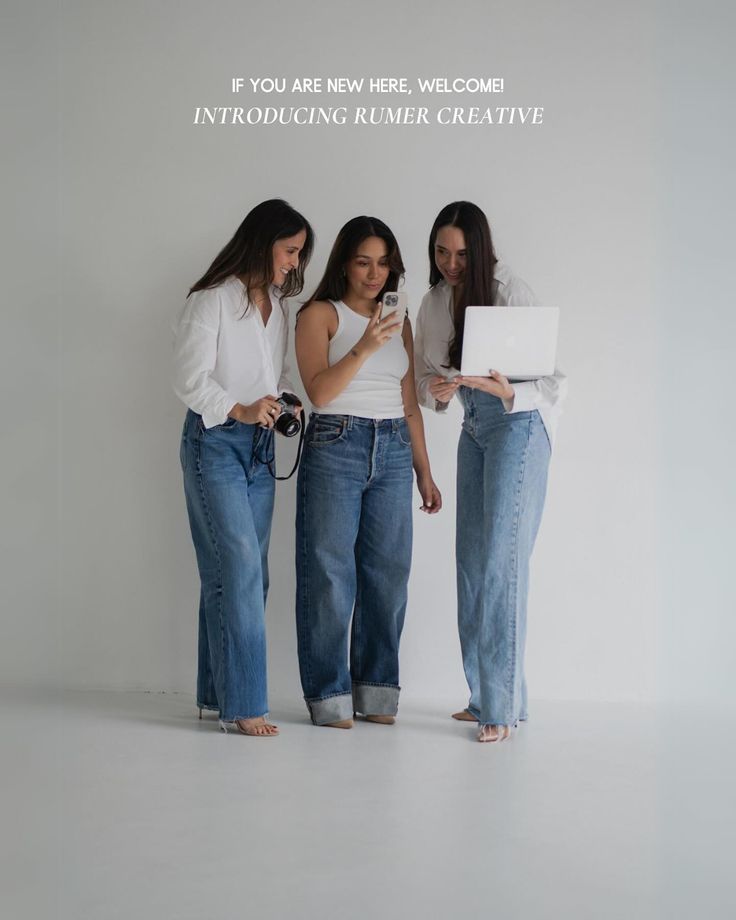 three women standing next to each other holding laptops and looking at their cell phones