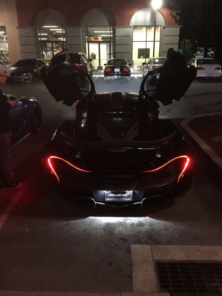 the back end of a black sports car parked in front of a building at night