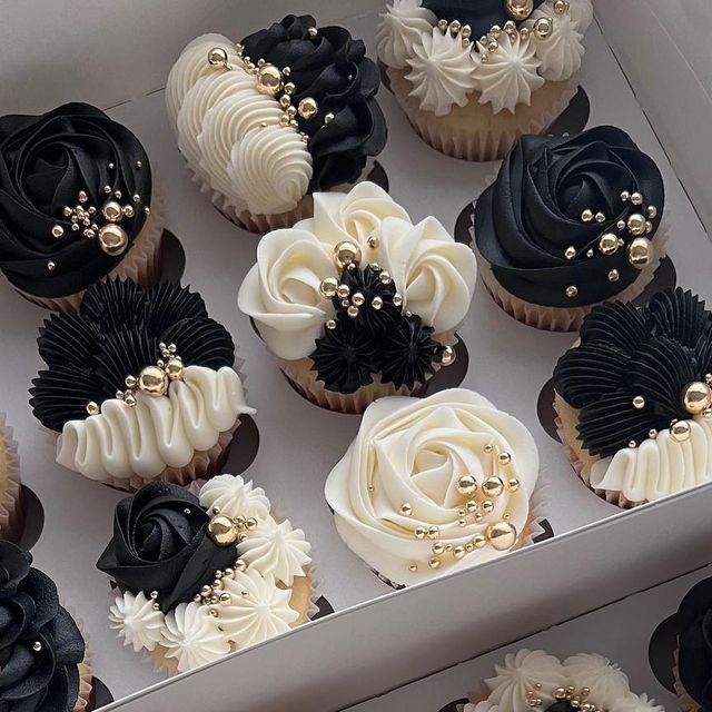 cupcakes decorated with black, white and gold icing in a display box