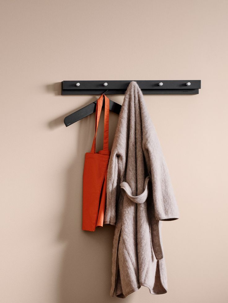 a coat rack with two coats hanging from it's hooks and an orange bag next to it