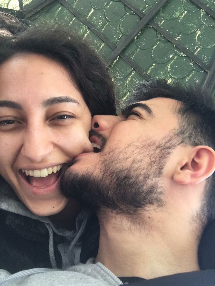 a man and woman kissing each other while laying on the ground in front of a fence