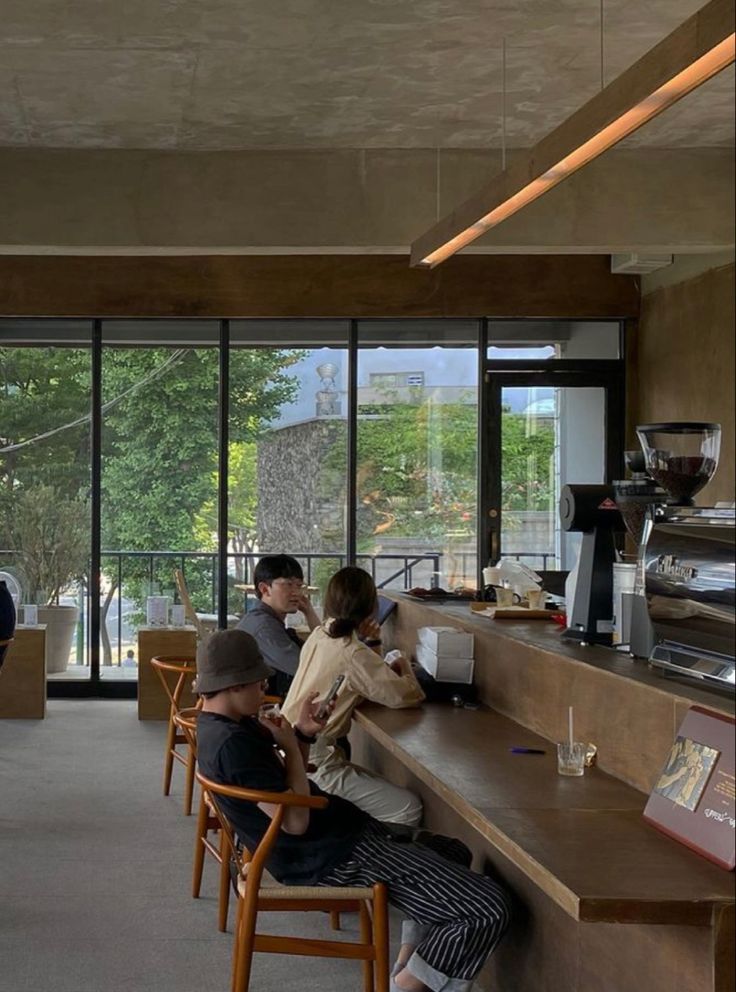 people sitting at tables in a restaurant with large windows looking out on the trees outside