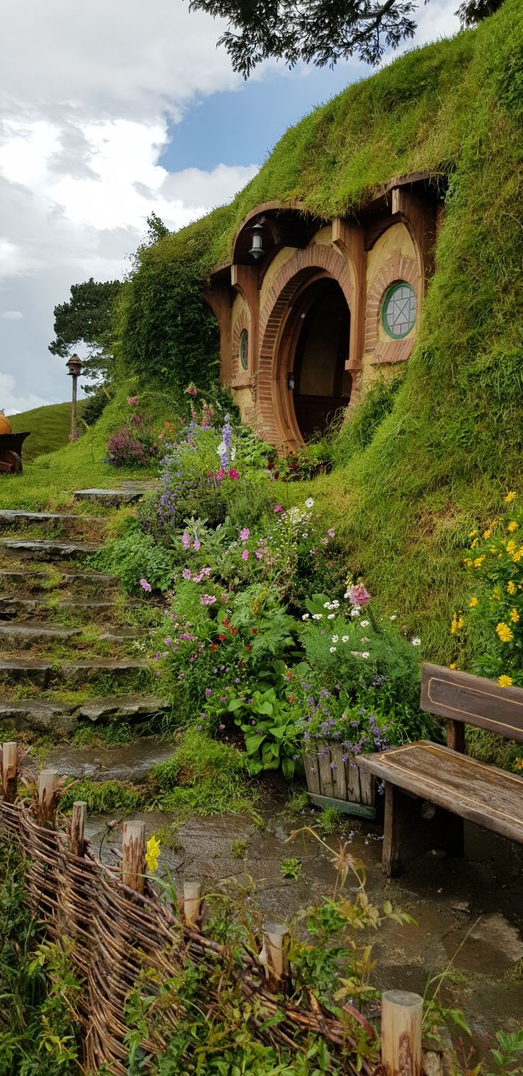 the hobbot house is surrounded by lush green grass and flowers, with stairs leading up to it