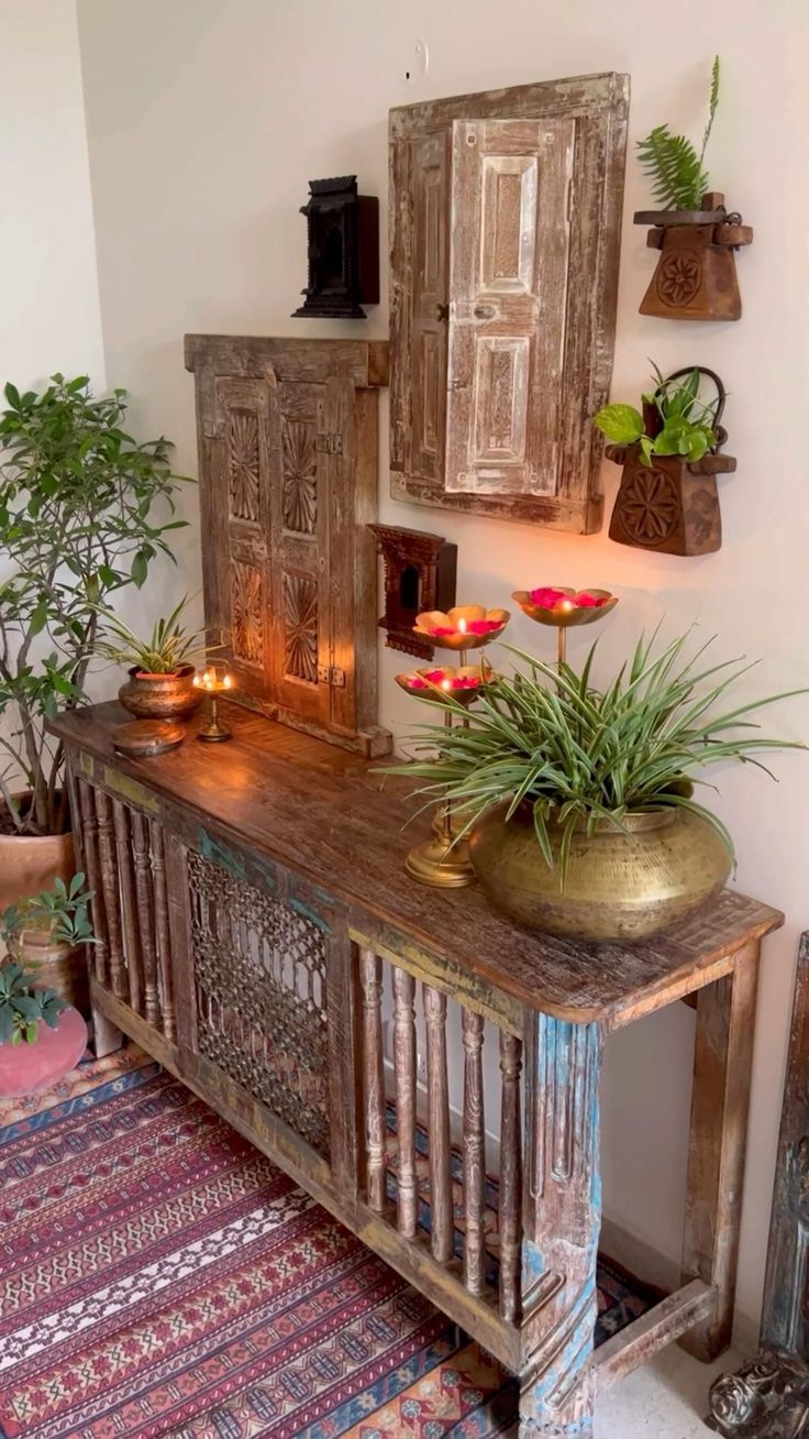 a wooden table topped with potted plants next to a wall filled with pictures and candles