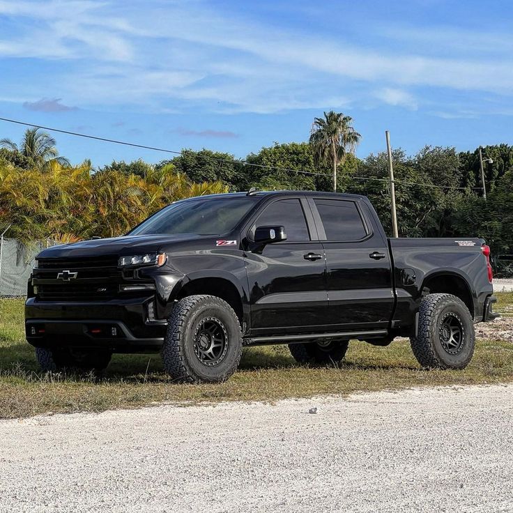 the black truck is parked on the side of the road in front of some trees