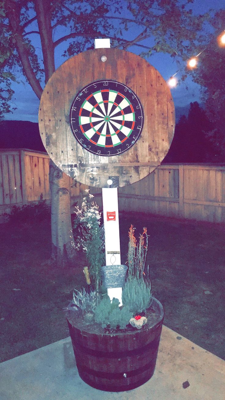 a dart board mounted to the side of a wooden barrel with plants in front of it