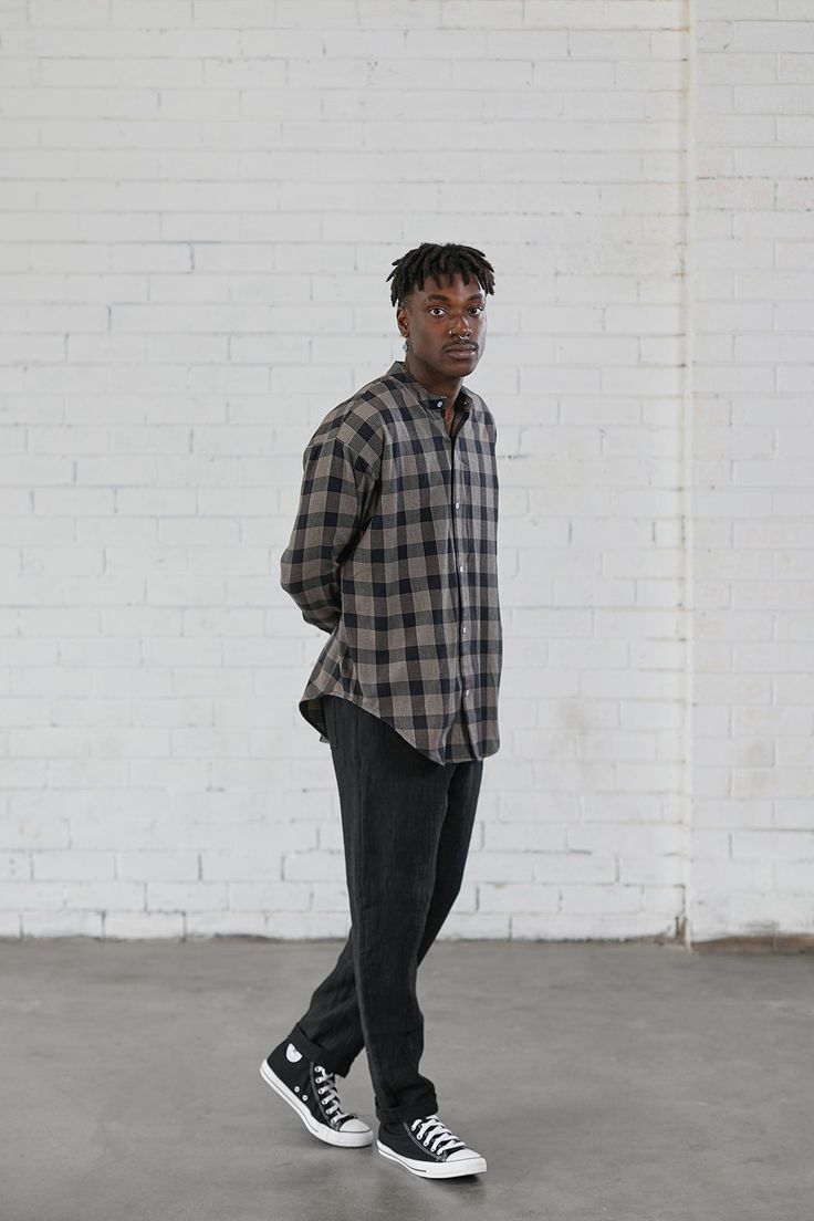 a man standing in front of a white brick wall with his hands in his pockets