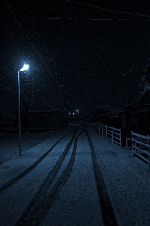 a street light in the middle of a snow covered road at night with no one on it