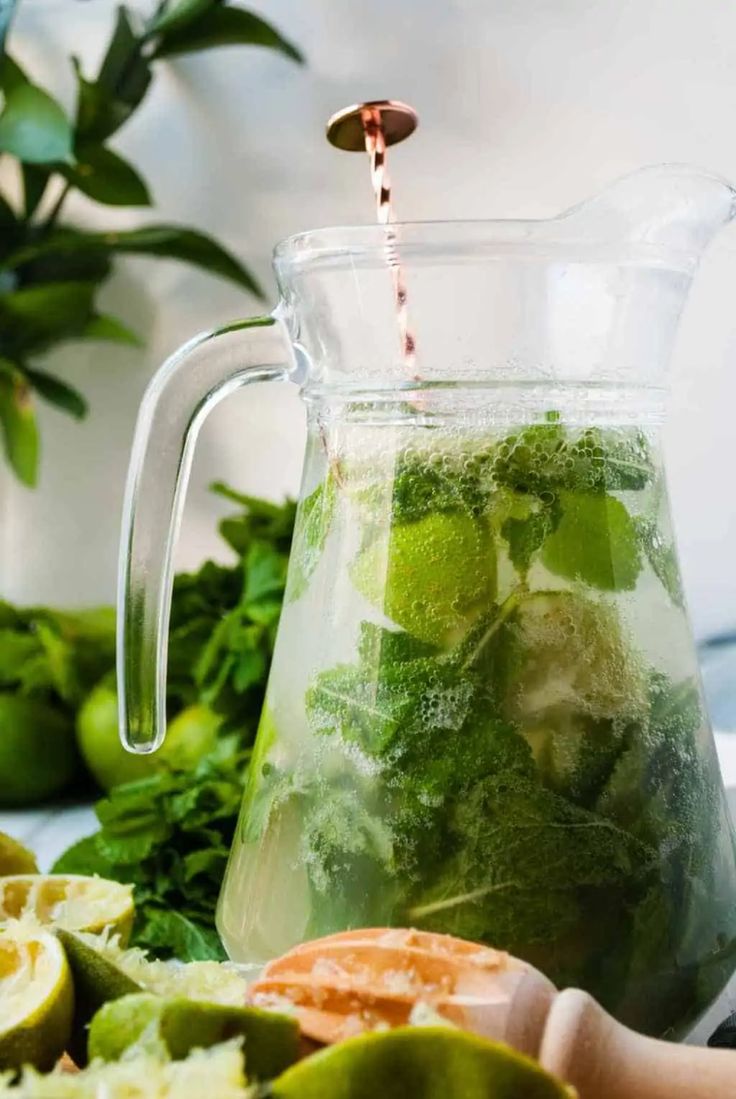 a pitcher filled with green liquid sitting on top of a table next to sliced oranges