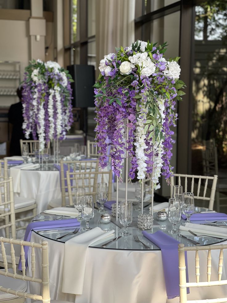 the table is set with purple and white flowers in tall vases on each side