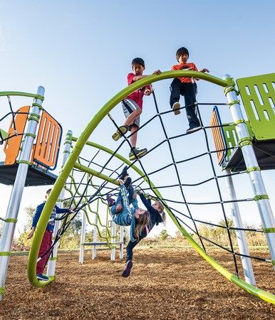 two children are climbing on the top of a play structure at a park, while another child is hanging upside down