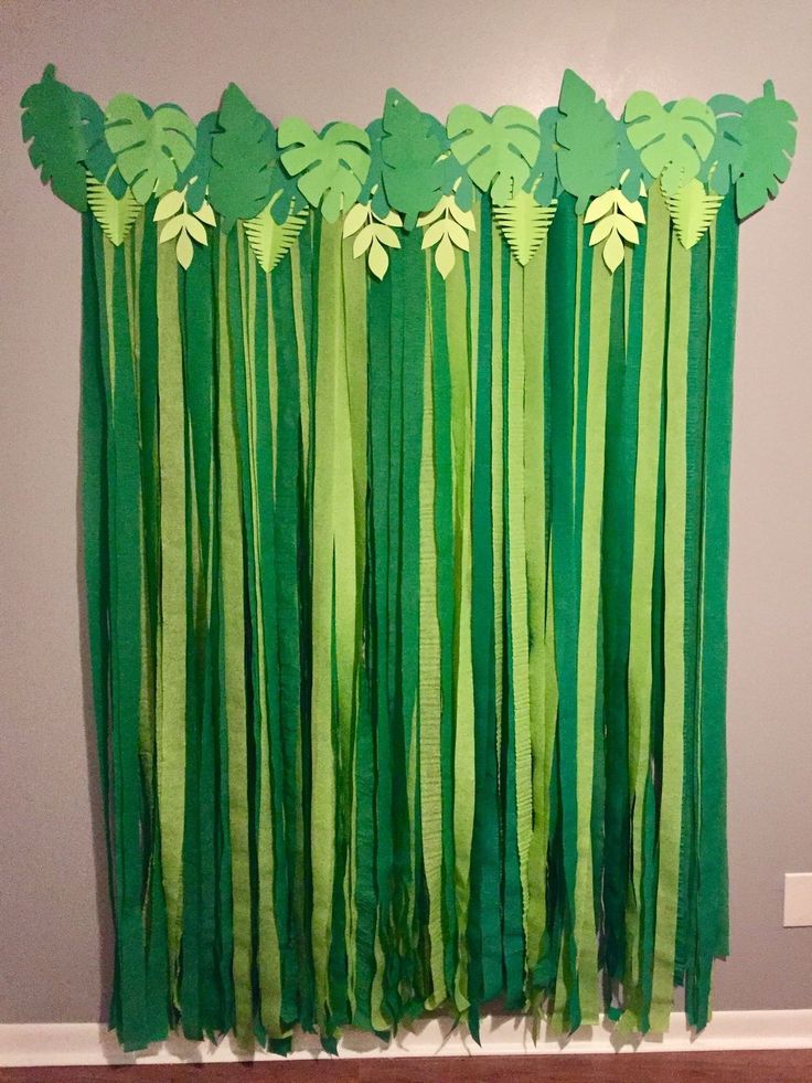 a green curtain with leaves hanging from it's side in front of a wall