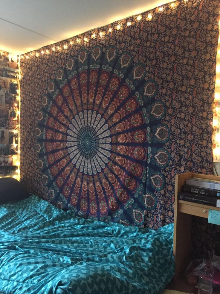 a bed with a blue comforter in front of a tapestry on the wall above it