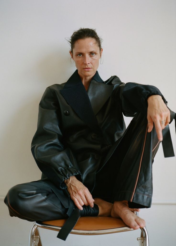 a woman sitting on top of a wooden table wearing a black coat and matching pants