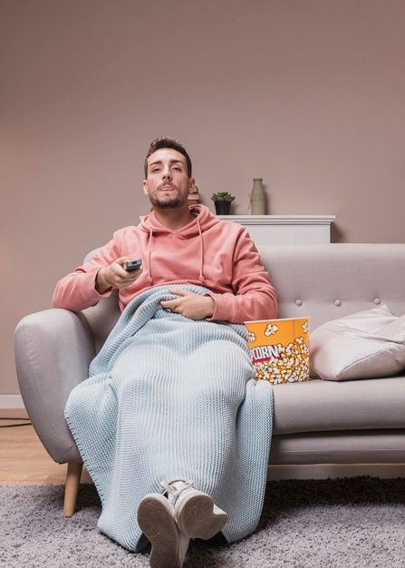 a man sitting on a couch holding a remote control and watching tv while eating popcorn