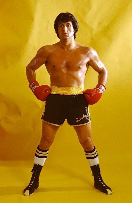 a man with boxing gloves on standing in front of a yellow background and posing for the camera