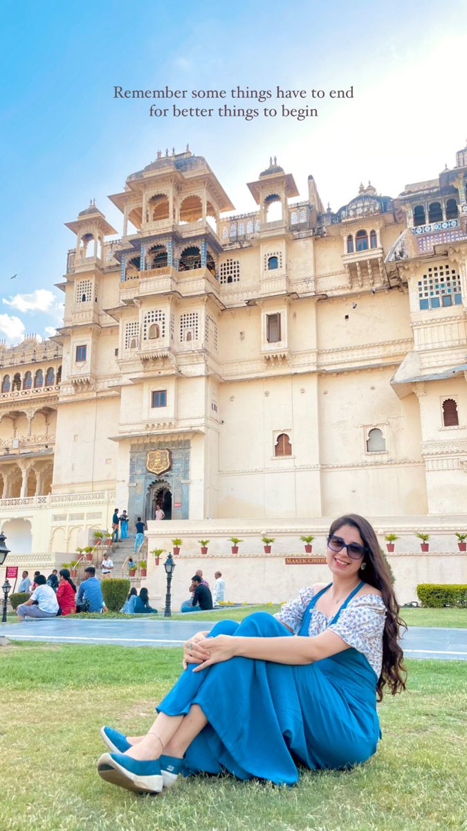 a woman sitting on the grass in front of a large building with words above it