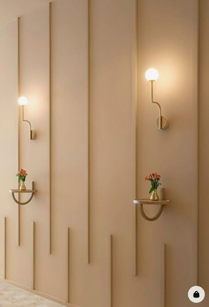 three lights are on the wall next to two vases with flowers and candles in them