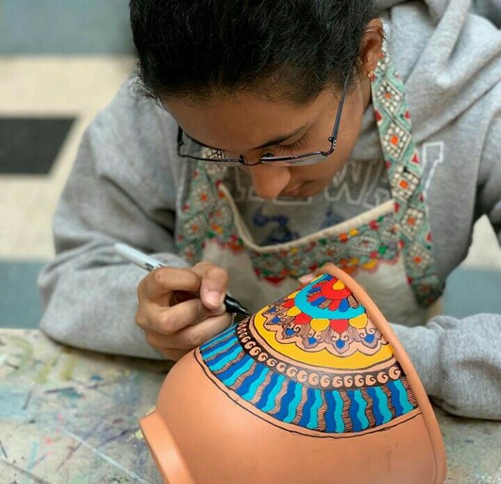 a young boy is working on a clay vase with his hands and face painted to look like an ornament