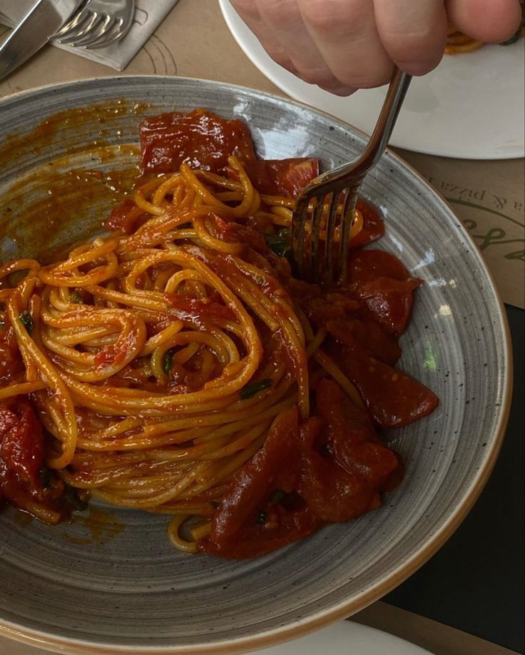 someone is eating spaghetti in a bowl with sauce on the side and a fork stuck into it