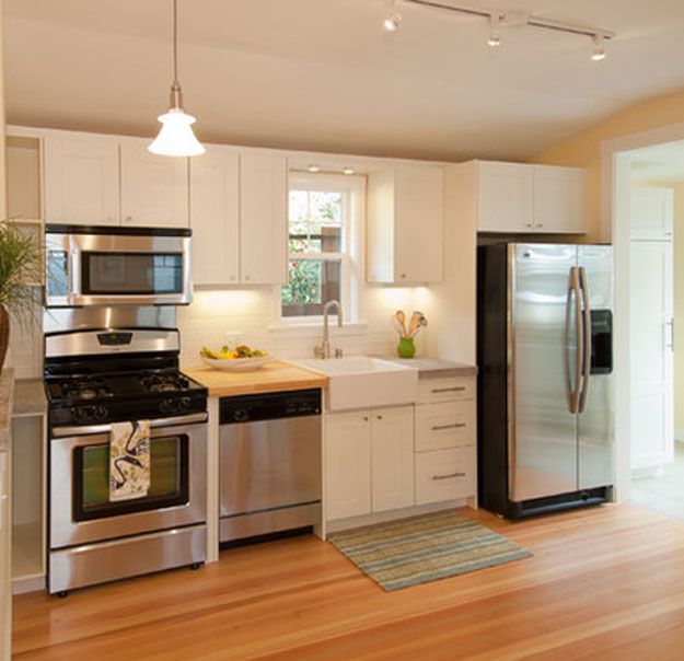 an open kitchen with stainless steel appliances and white cabinetry, hardwood flooring, potted plant on the counter