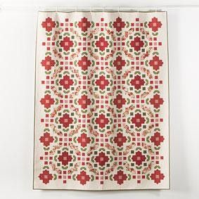 a red and white quilt hanging on the wall next to a curtain with flowers in it