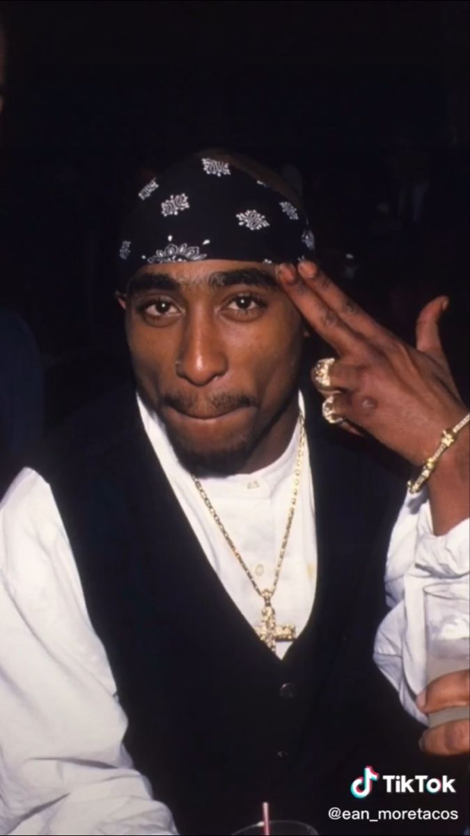 a man in a black vest and bandana holding his hand up to his face