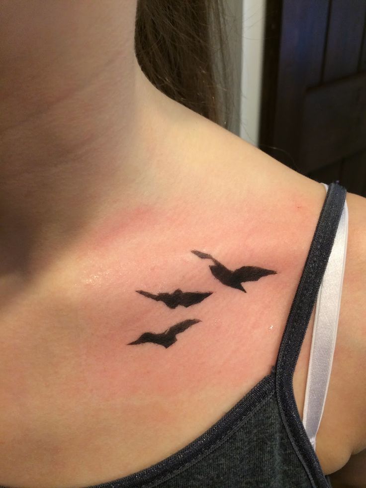 a woman's neck with three birds flying in the sky on her left side