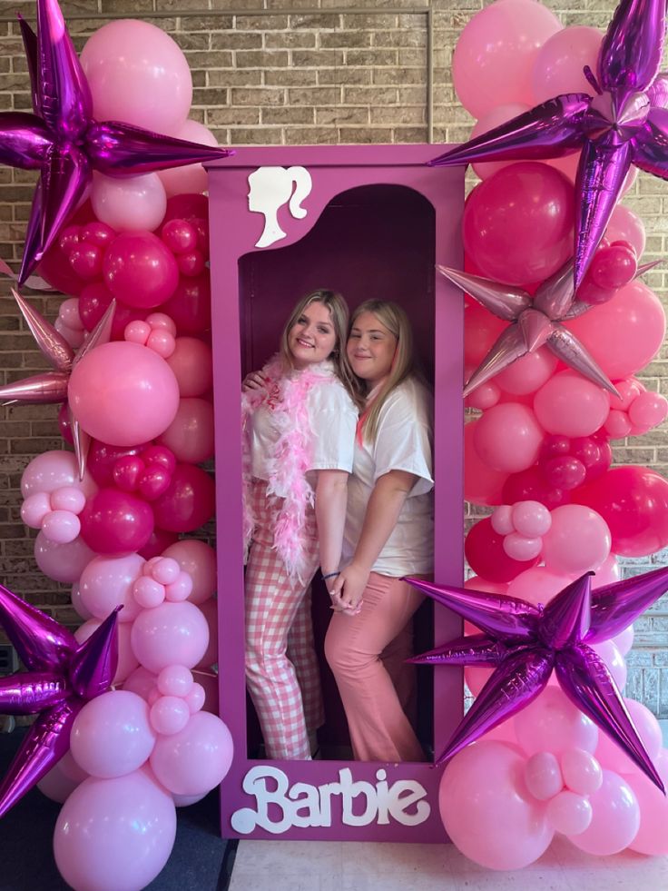 two women standing in front of a photo frame with balloons