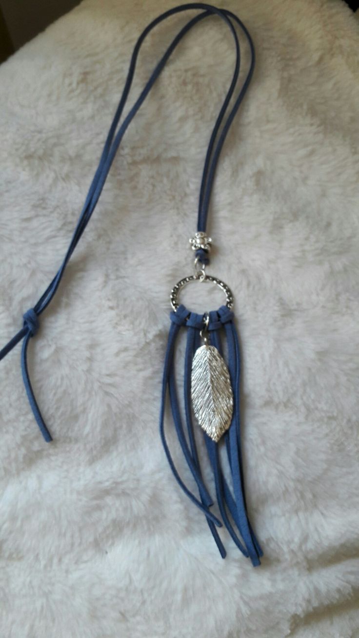 a blue necklace with silver leaves on it sitting on top of a white fur covered surface